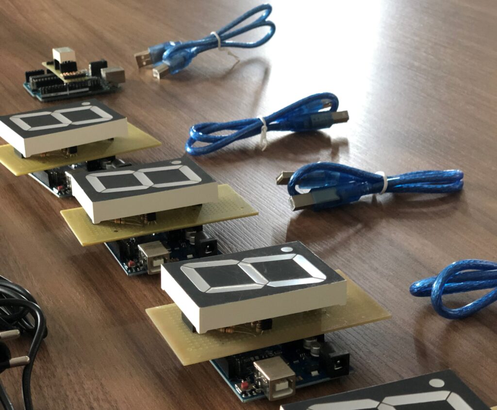 Kits de Arduinos em cima de uma mesa. São placas eletrônicas com display de 7 segmentos (para exibição de números).