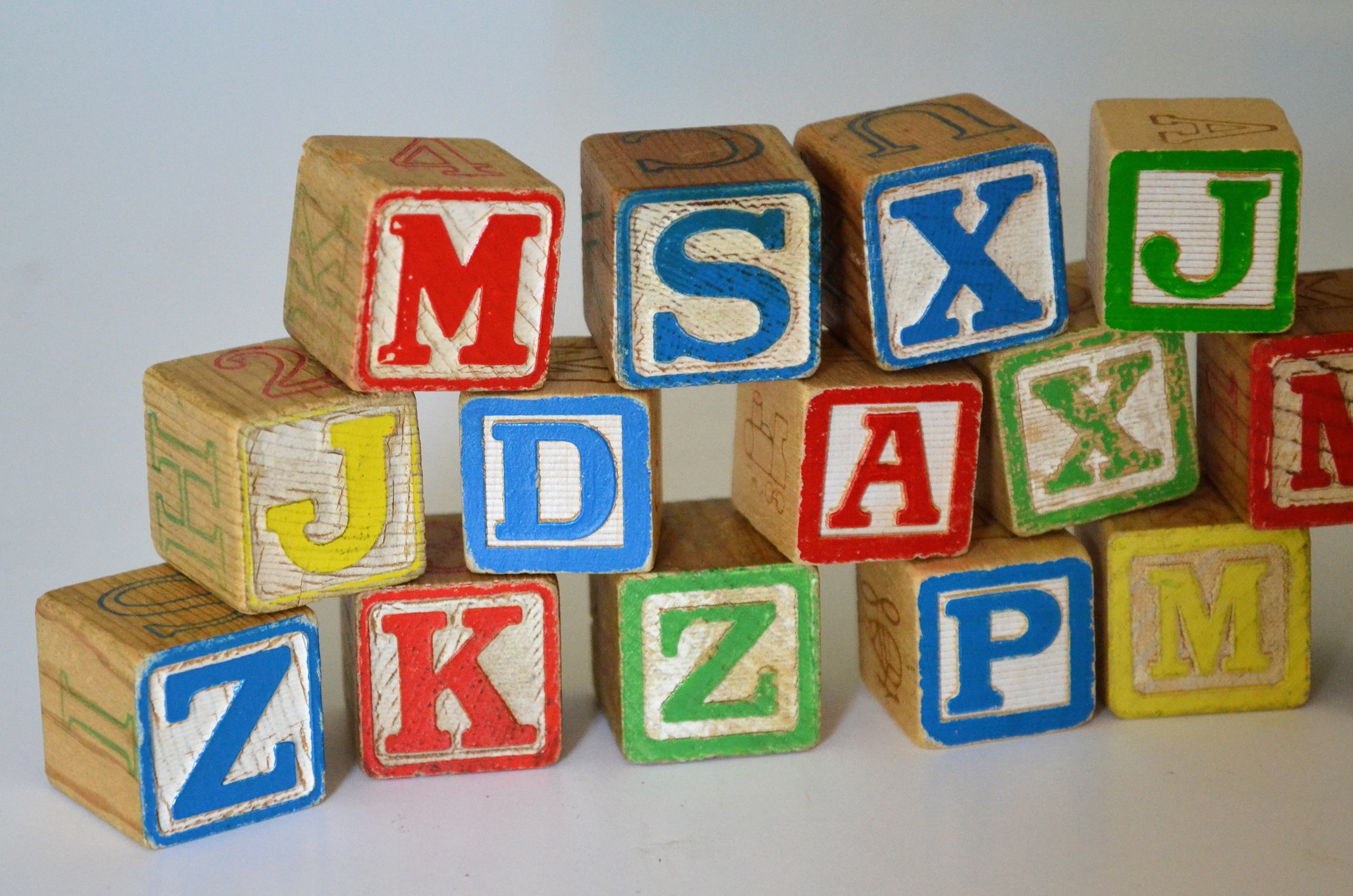 Blocos de madeira coloridos empilhados, cada um com uma letra diferente do alfabeto.