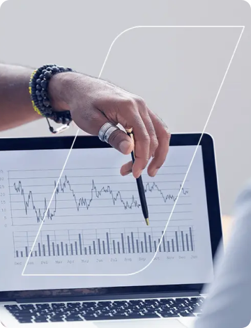 Photo of a hand holding a pen, pointing at a graph on a notebook screen.