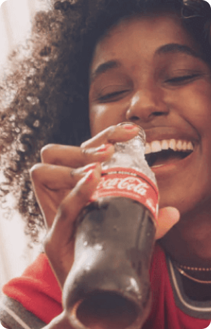 Photo of a woman about to drink Coca-Cola from a glass bottle.