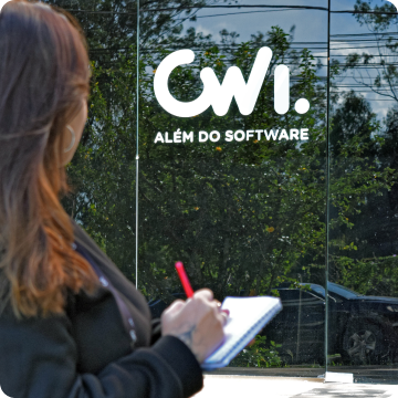 Foto em área externa de uma mulher de costas segurando um bloco e uma caneta, olhando para o logotipo da CWI - Além do Software em uma porta de vidro.