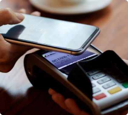 Foto de uma pessoa usando um smartphone para pagar uma compra em um terminal de pagamento.
