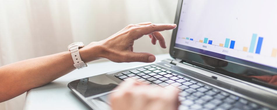 A hand pointing to charts on a laptop screen.