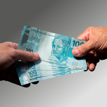 Photo of a hand handing over five 100 Brazilian reais banknotes.