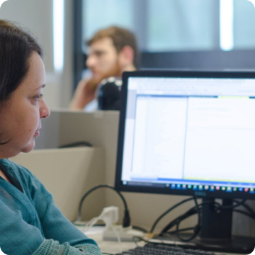 A imagem mostra uma mulher branca olhando para a tela de um computador.