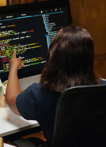 Uma mulher de costas apontando para um monitor com código em tela.