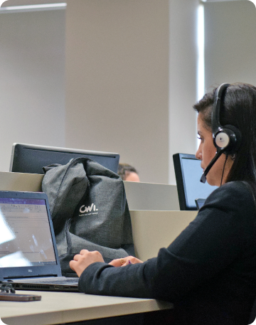 Uma mulher usando um headset trabalha em frente a um notebook, com uma mochila da CWI sobre a mesa.