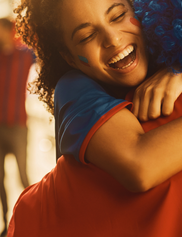 Pessoa sorridente abraçando alguém com peruca azul, em ambiente alegre com filtro gráfico em tons de vermelho.