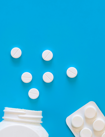 Comprimidos brancos espalhados sobre fundo azul com frasco e blister.