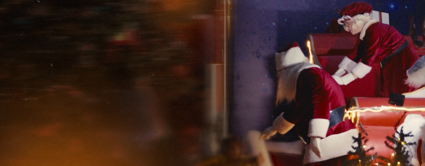 Personagens vestidos de Papai Noel organizam presentes em um trenó iluminado, em uma cena natalina com clima festivo.