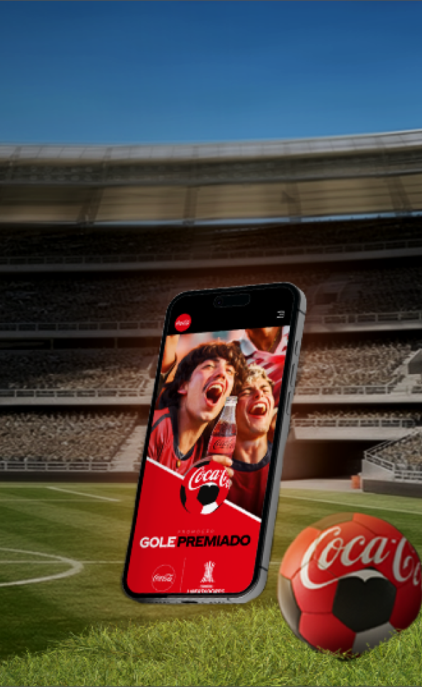 O fundo mostra um estádio de futebol e, sobre o gramado, está um celular e uma bola de futebol da Coca-Cola.