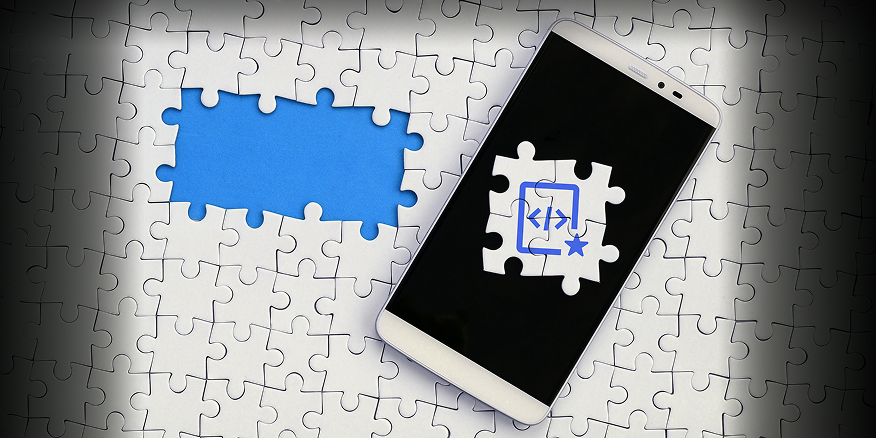 A imagem mostra um homem de costas, sentado em frente a um computador em um ambiente de escritório. Ele tem cabelos escuros, usa uma camisa xadrez e fones de ouvido pretos da marca JBL. Na tela do monitor, é possível ver a interface de um programa de edição ou código, com o ícone do VS Code em destaque. O ambiente ao redor é claro e profissional, passando uma sensação de foco e trabalho.